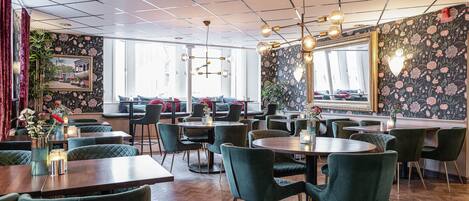 Un restaurant avec des chaises à revêtement vert, des tables en bois et un papier peint à motifs floraux.