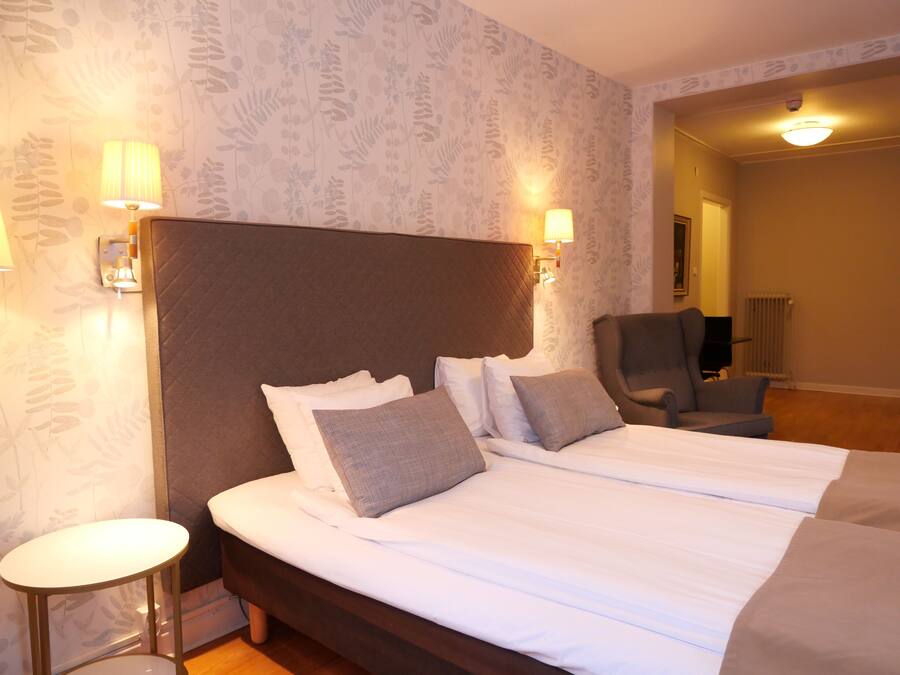 Habitación de hotel con una cama grande, dos lámparas de noche, una silla y un radiador.