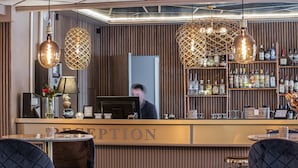 A reception area with a wooden panel wall, a reception desk, and two hanging pendant lights. - Hotell Arkad (Vasteras)