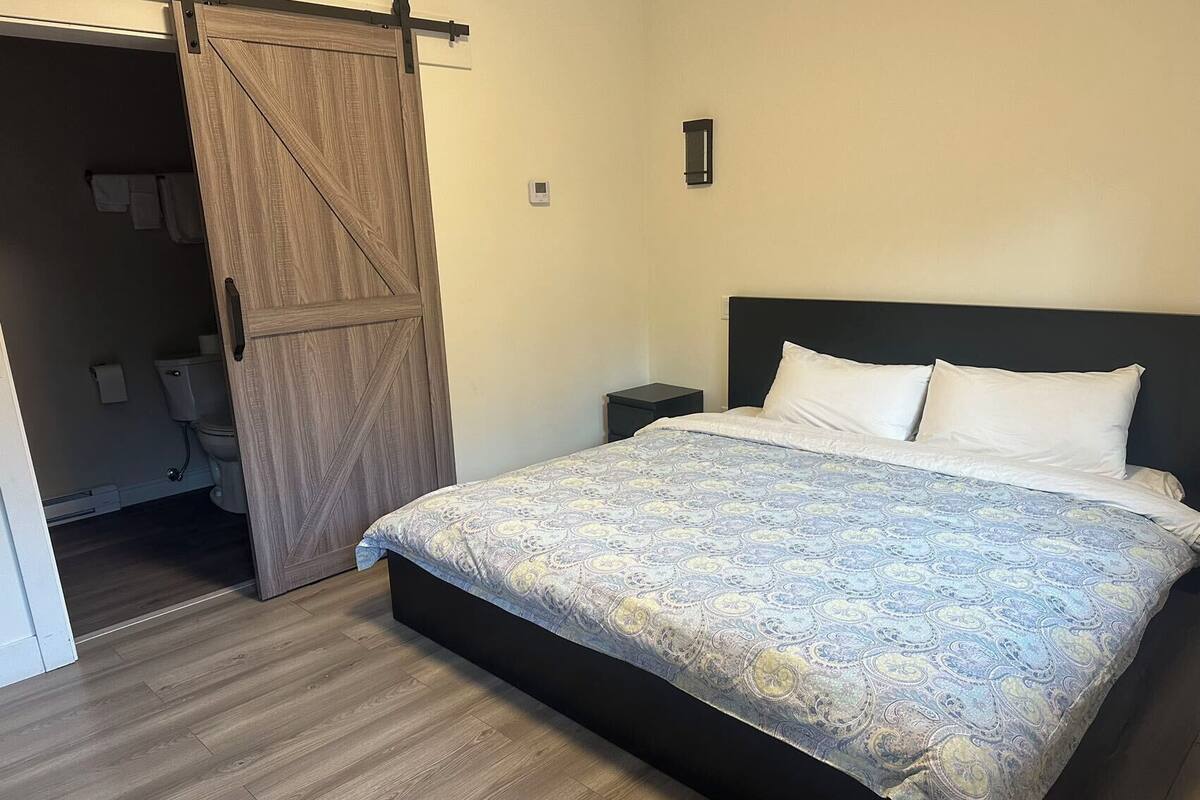 A bedroom with a bed, a nightstand, a wall-mounted light, and a sliding door leading to a bathroom.