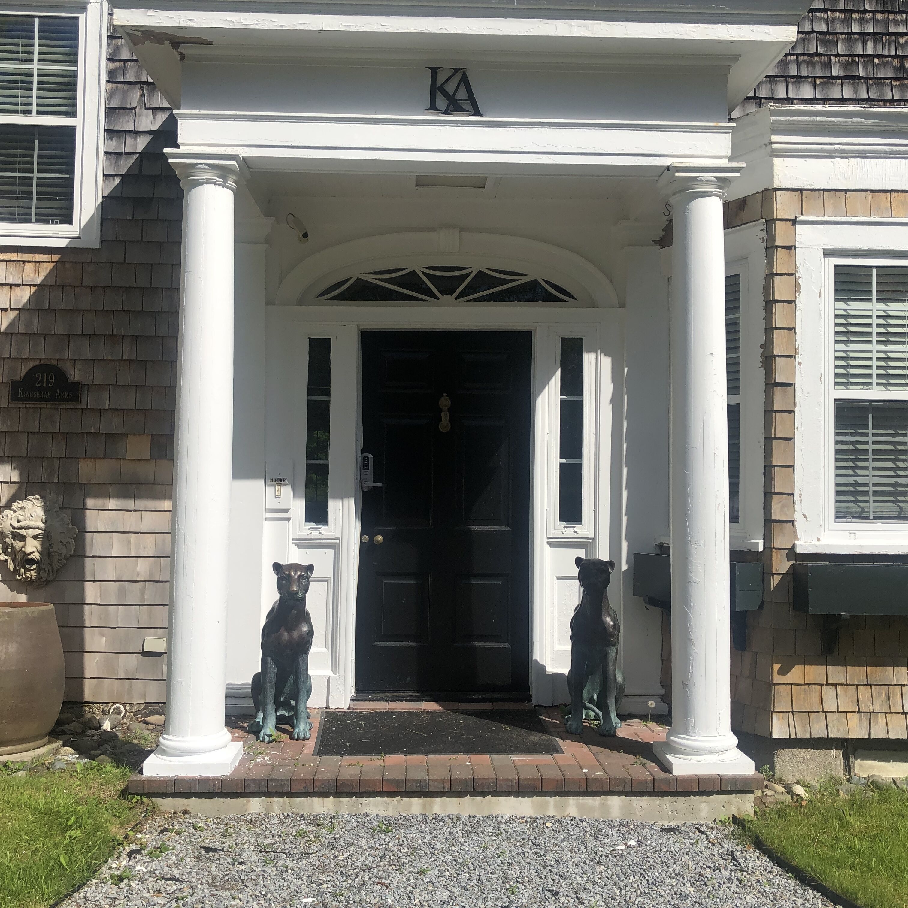 A building entrance with a black door, white columns, and two dog statues.