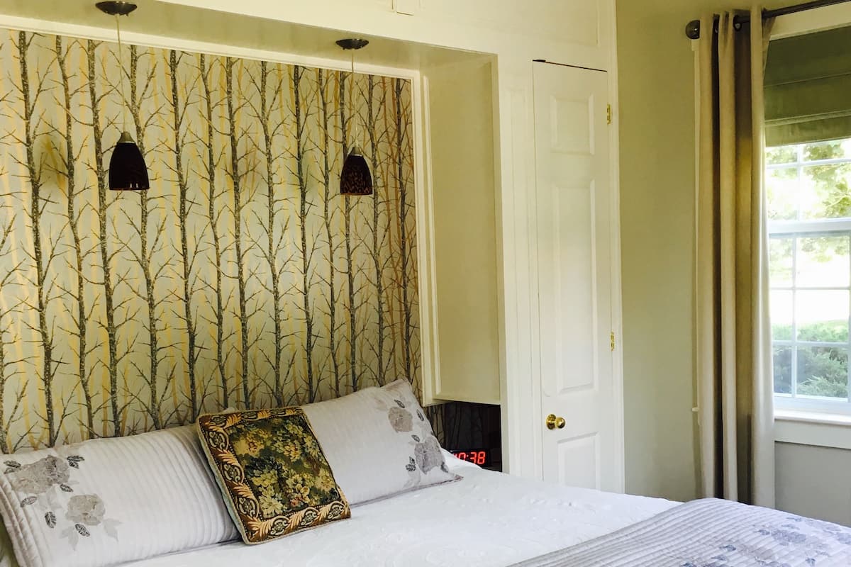 Une chambre à coucher avec un lit, deux lampes fixées au mur, une porte et une fenêtre avec des rideaux.