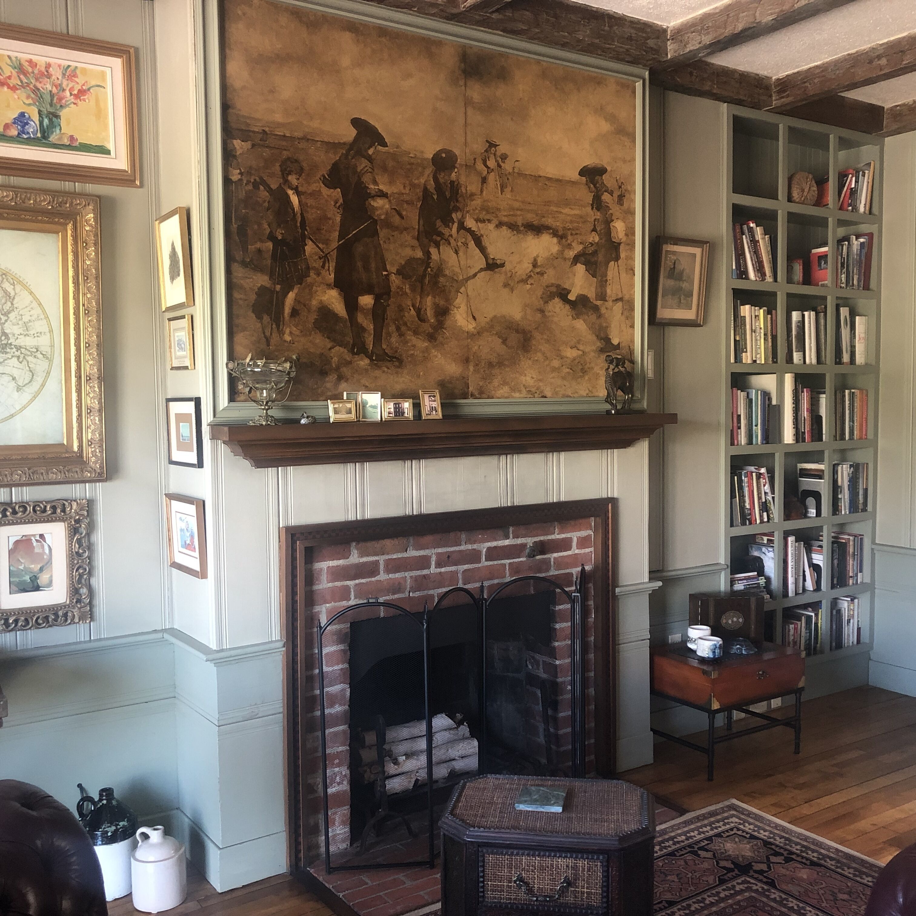 A room with a fireplace, bookshelves, and framed artwork.
