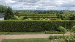 Ein angelegter Garten mit ordentlich geschnittenen Hecken, einem gepflasterten Weg und einem kleinen weißen Gebäude.