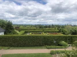 A landscaped garden with neatly trimmed hedges, a paved walkway, and a small white building.