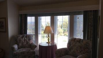 A room with two floral armchairs, a small round table with a lamp, and a window with blinds.