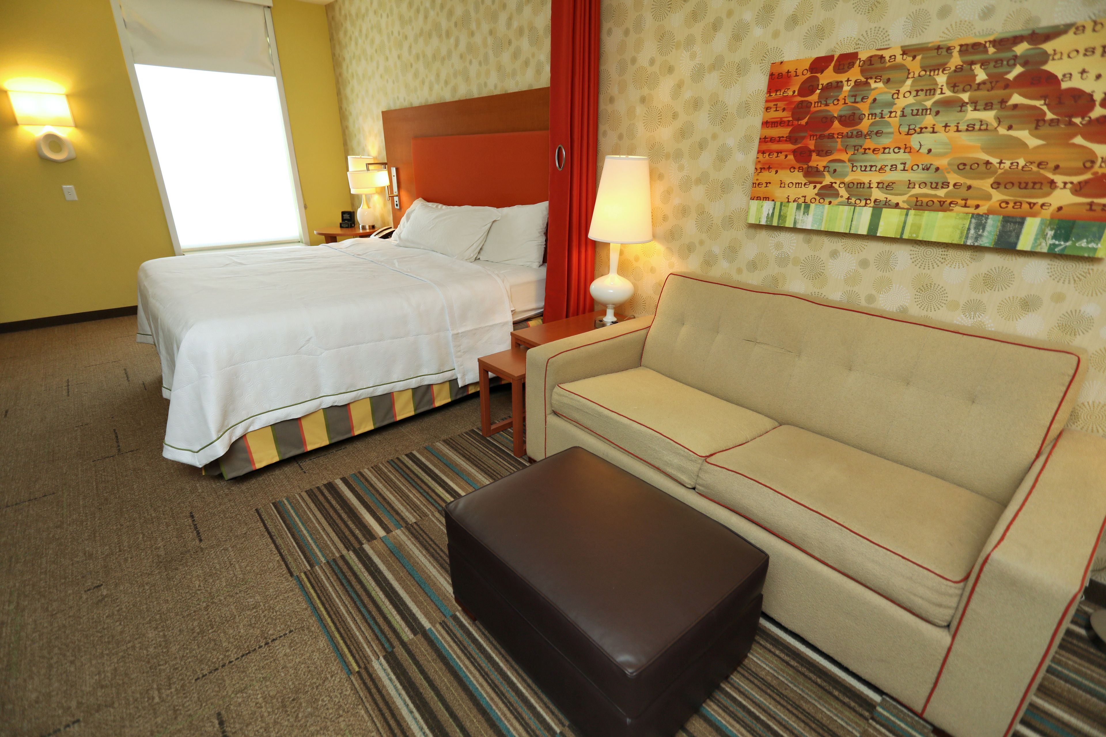 A hotel room with a bed, a sofa, a nightstand, a lamp, and a map on the wall.