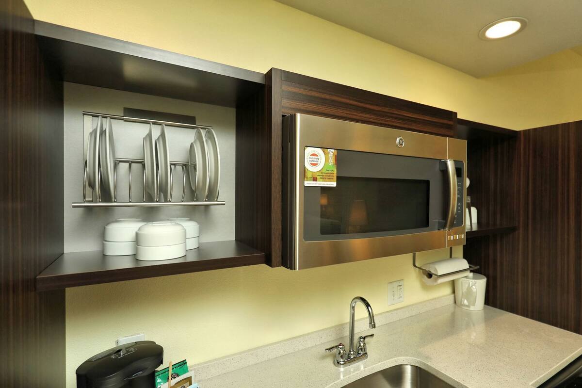 Een moderne keuken met een ingebouwde magnetron, roestvrijstalen apparatuur en een spoelbak.