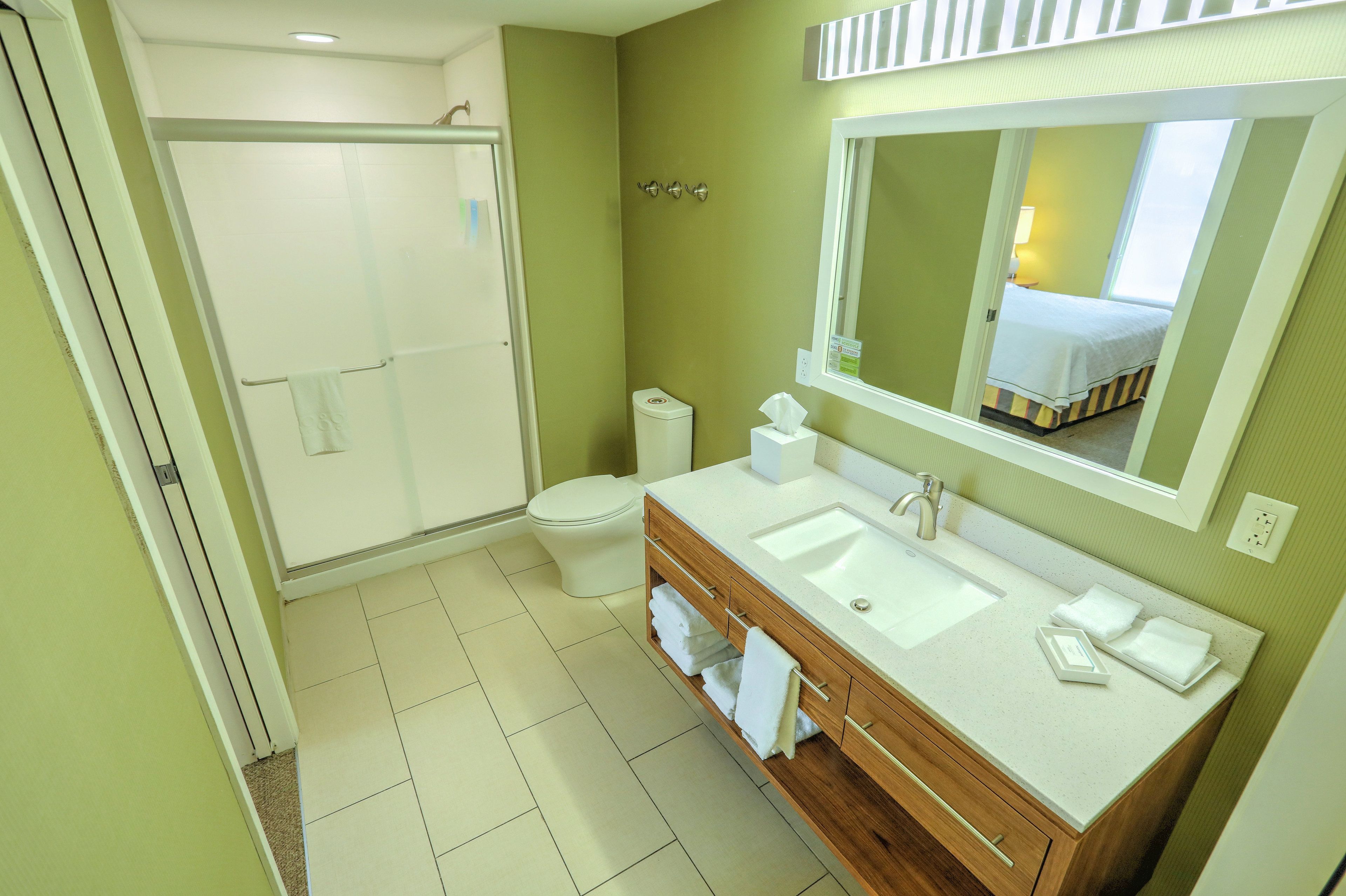A bathroom with a shower, toilet, sink, and a mirror.
