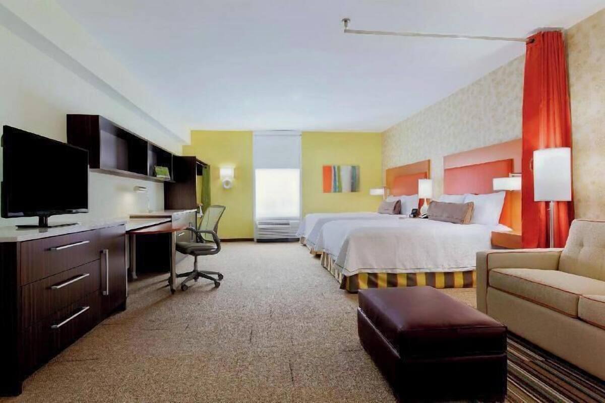 Hotelkamer met een bureau, televisie, twee bedden, een bank en een groot raam.