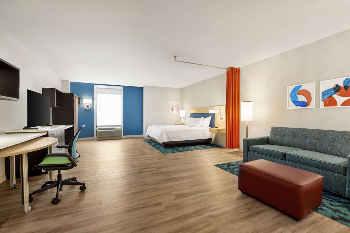 Una habitación de hotel con cama, sofá, escritorio con silla, televisor y obras de arte en la pared.