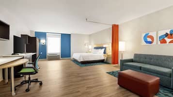 A hotel room with a bed, a sofa, a desk with a chair, a television, and artwork on the wall.