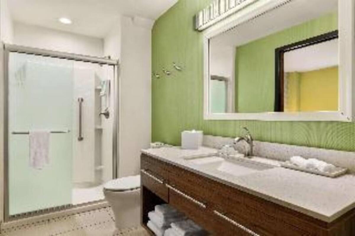 Un baño con cabina de ducha de vidrio, tocador con espejo y lavamanos.