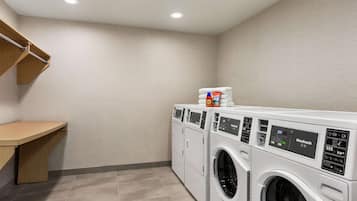 A laundry room with a wooden bench, two front-loading washing machines, and a stacked pile of white towels.