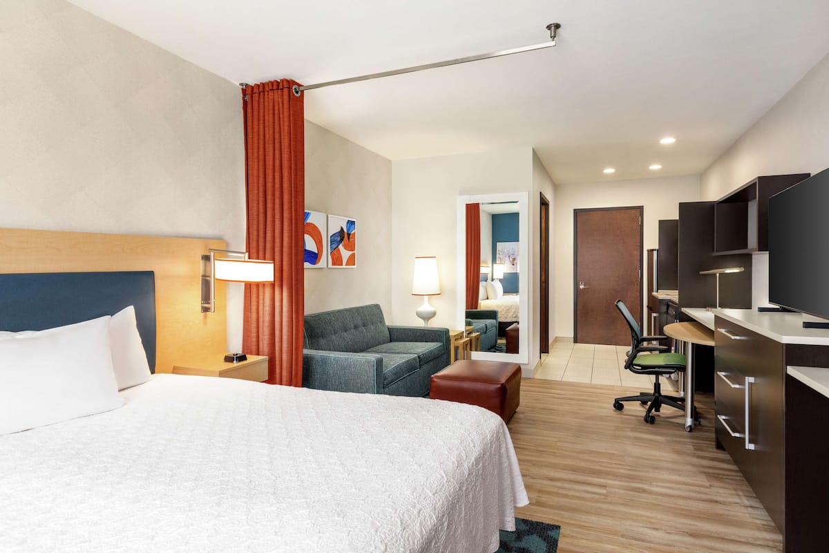 Habitación de hotel con una cama grande, un escritorio con una computadora, una silla y un televisor.