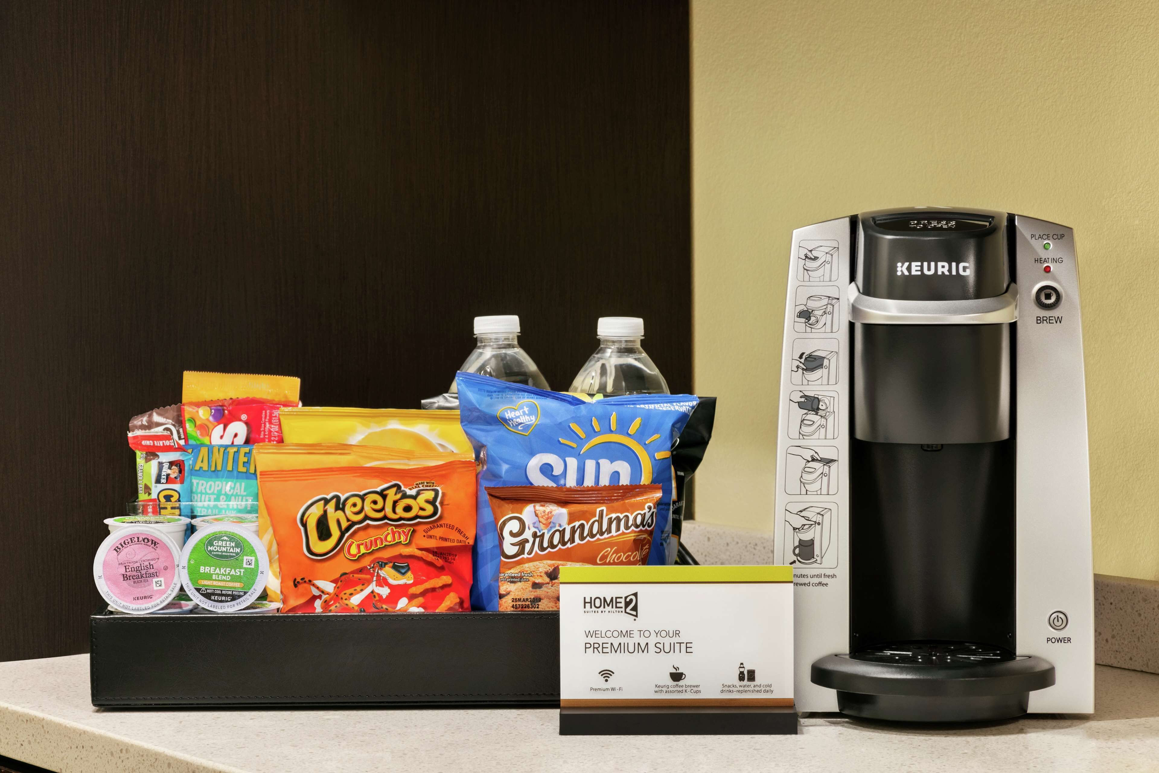 A coffee maker, a box labeled "HOME2 PREMIUM SUITE," and a snack tray with various items.