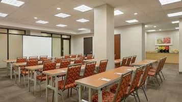 Uma sala de conferências com várias mesas e cadeiras, um quadro branco e uma área de cozinha.