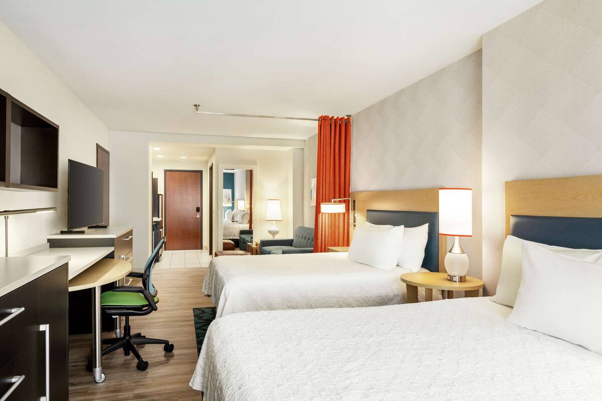 Una habitación de hotel con dos camas, un escritorio, una silla, un televisor y una lámpara.