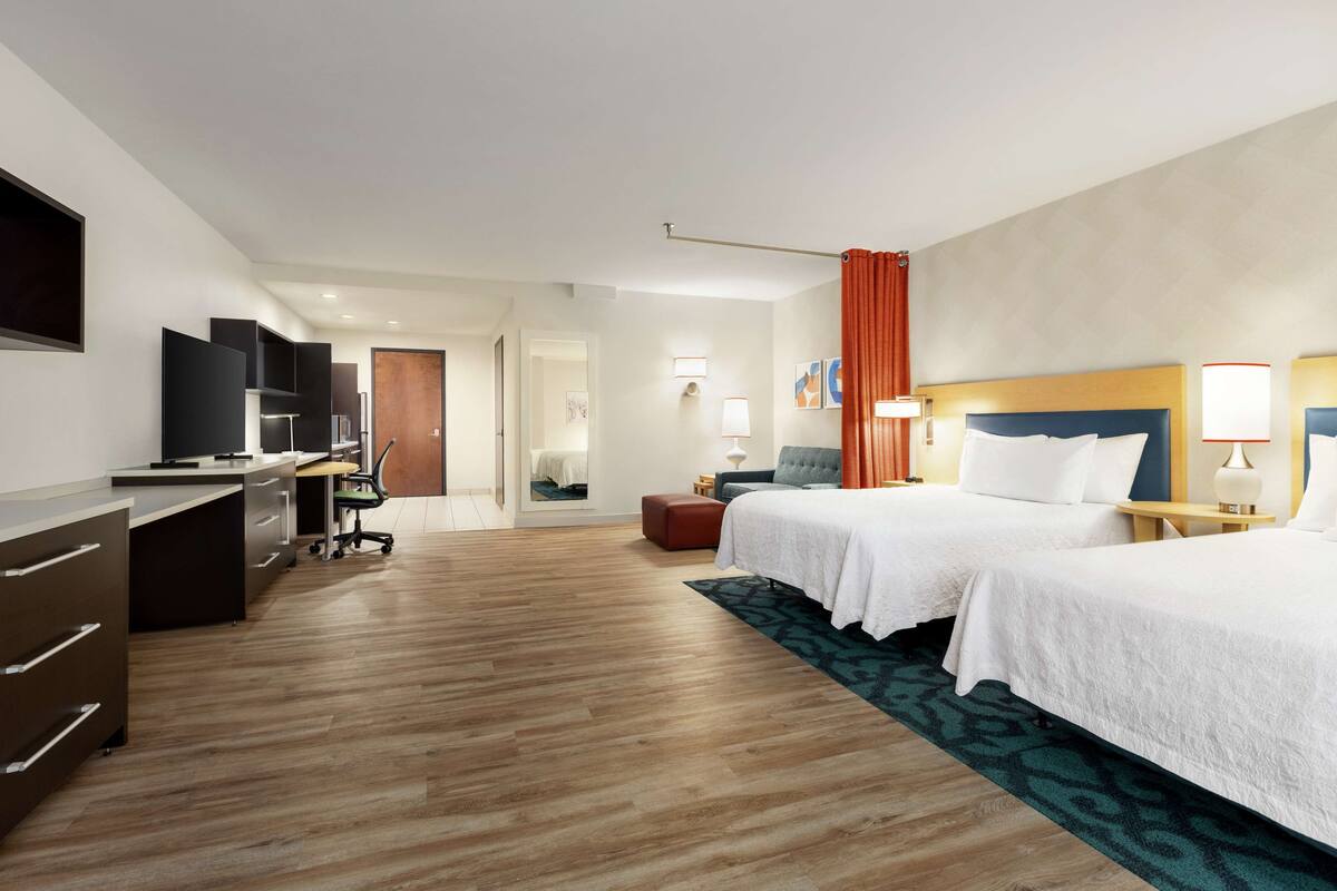 Habitación de hotel con dos camas, un escritorio, una silla y un televisor.