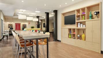 A modern kitchen with a long counter, bar stools, and a built-in TV. There are decorative items on shelves and a red door in the background.