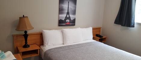 Habitación de hotel con una cama, una mesita de noche con lámpara, un teléfono, un cabecero de madera y una imagen de la Torre Eiffel en la pared.