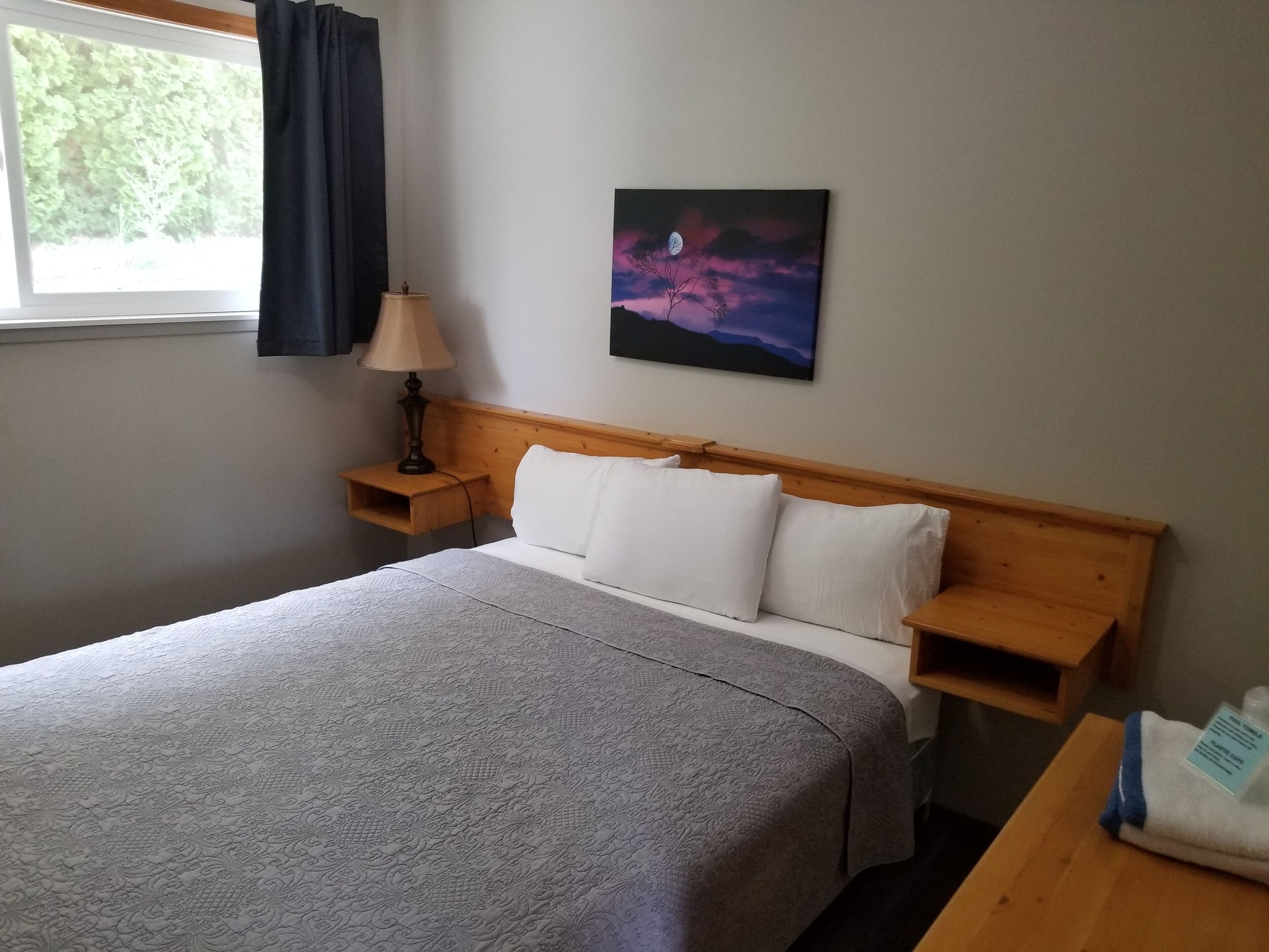 A neatly made bed with a grey bedspread, a wooden headboard, and a nightstand with a lamp.