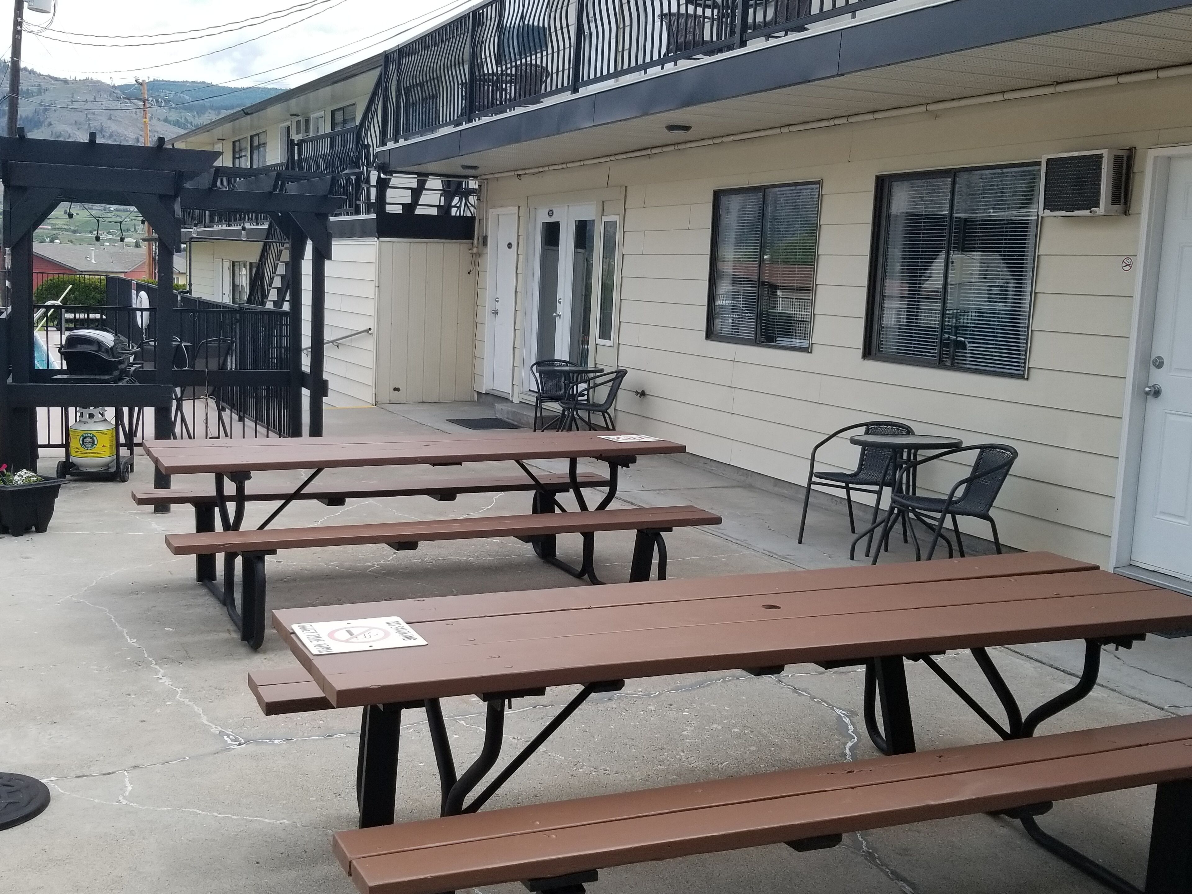 An outdoor patio with picnic tables and chairs, a covered seating area, and a building with a balcony.