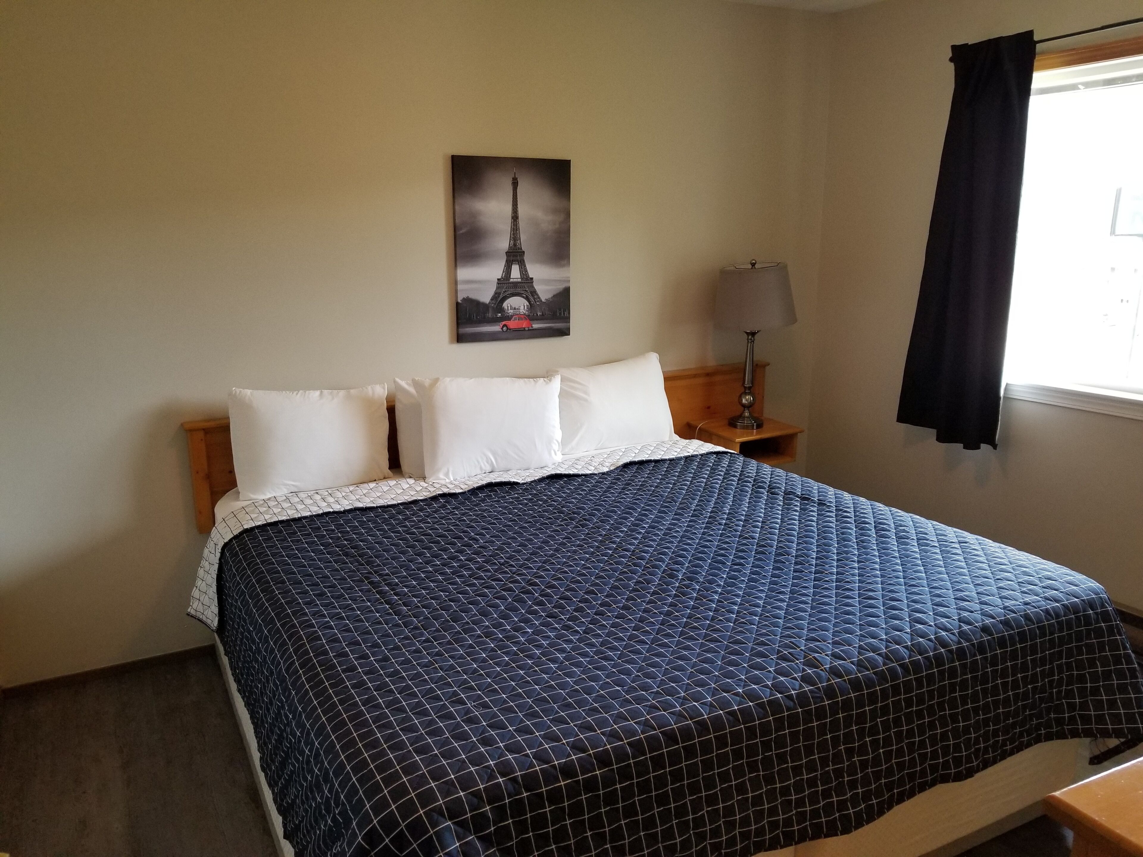 A neatly made bed with a patterned bedspread, a pillow, and a wall-mounted picture of the Eiffel Tower.
