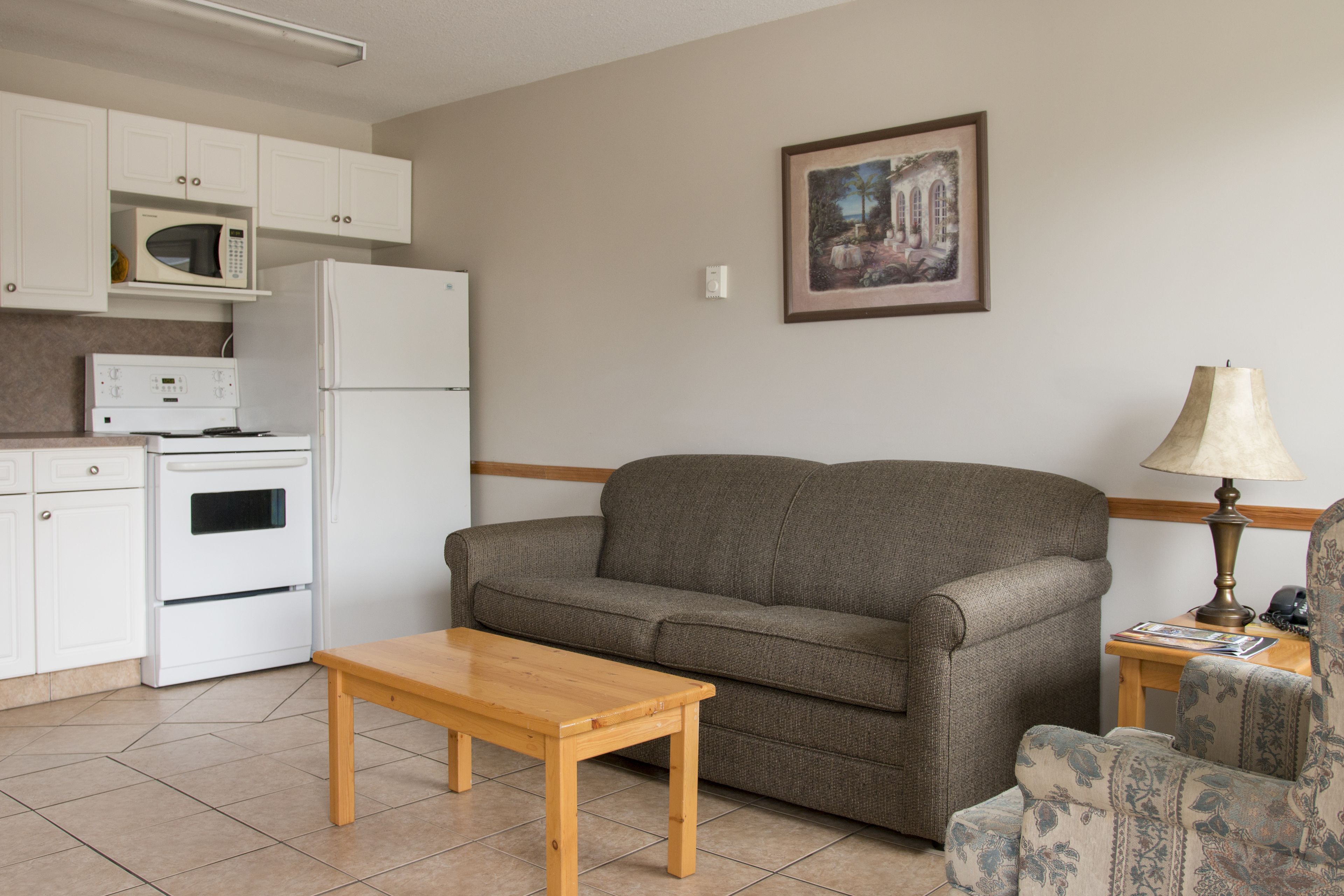Un espace de vie compact comprenant un coin cuisine, un canapé, une table en bois et un fauteuil à motifs.