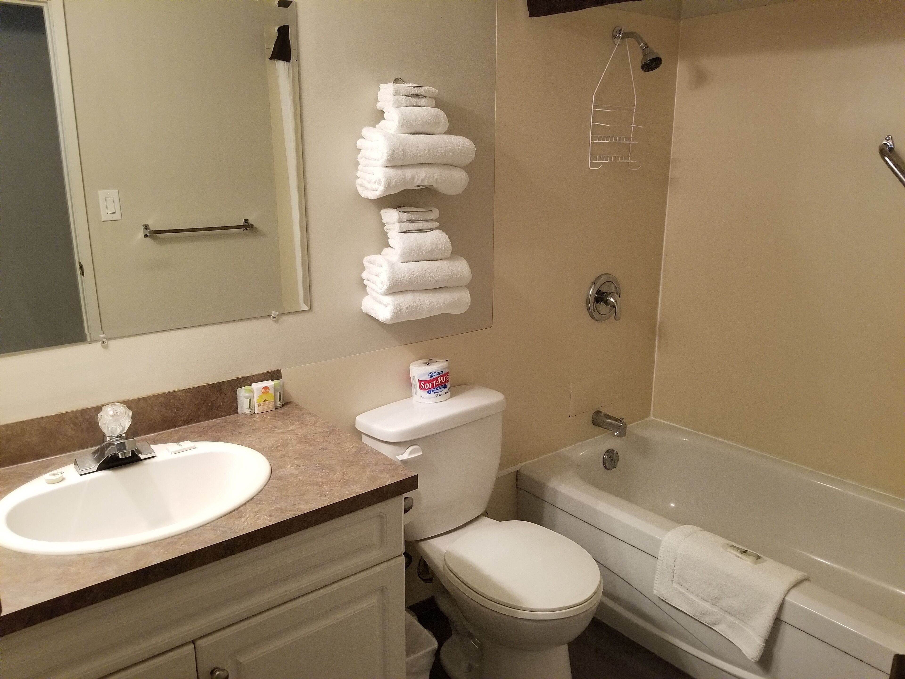 A bathroom with a sink, toilet, and bathtub. There are towels stacked on the wall and a showerhead above the bathtub.