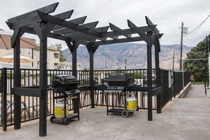 A covered outdoor grilling area with a view of mountains in the background. - Osoyoos Lakeview Inn & Suites (Osoyoos)