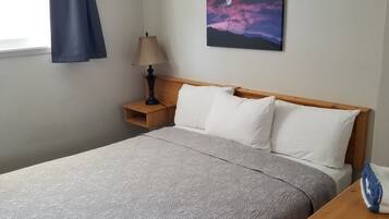 Ein ordentlich gemachtes Bett mit einem gemusterten Überwurf, einer Nachttischlampe und einem Gemälde einer mondbeschienenen Landschaft an der Wand.