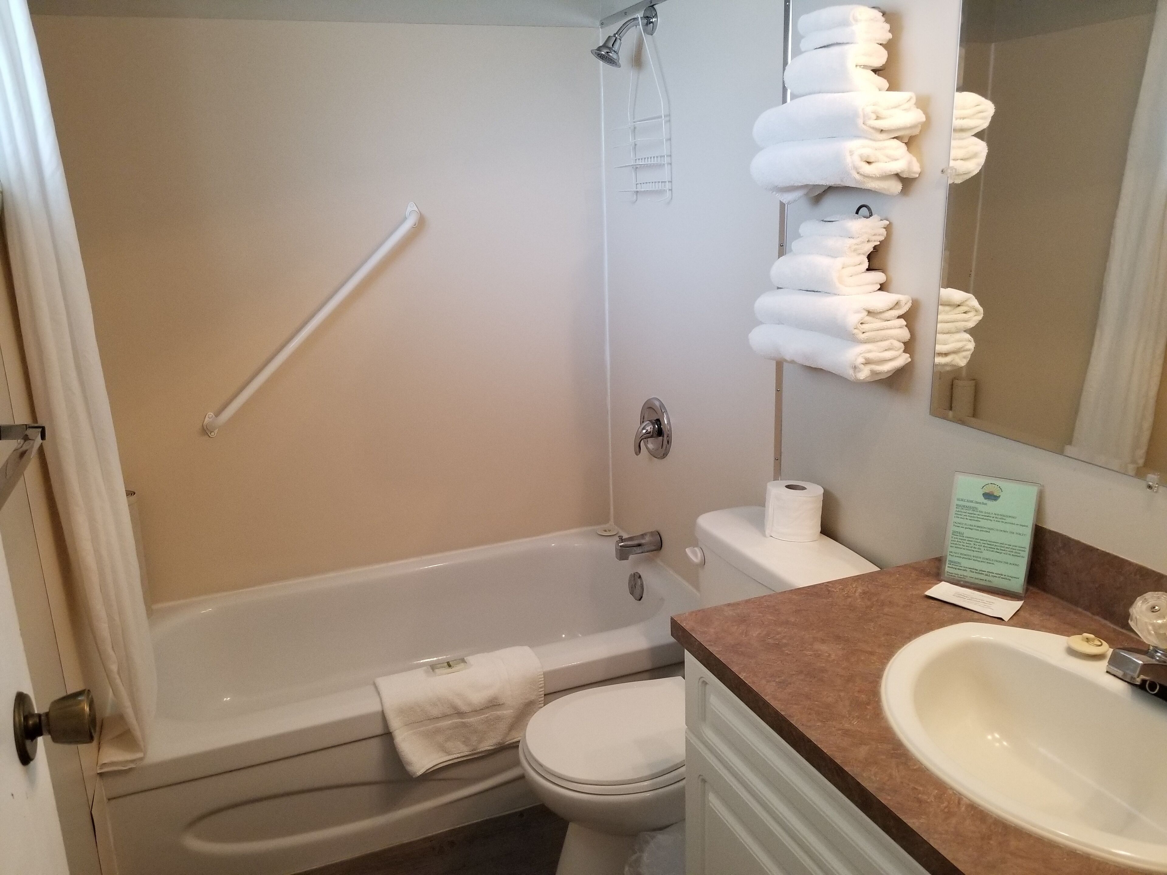 A bathroom with a bathtub, toilet, sink, and a towel rack with neatly folded towels.
