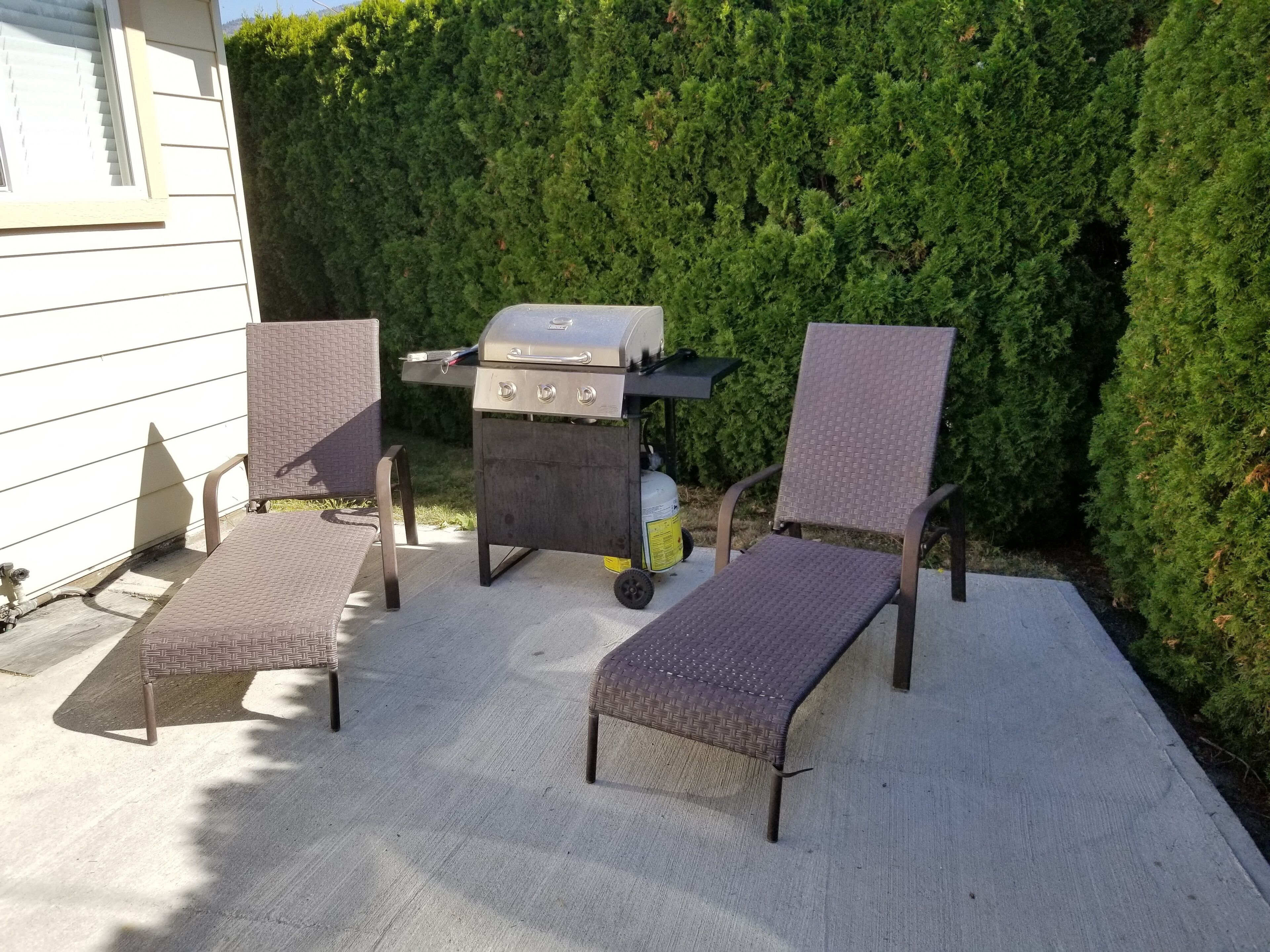 An outdoor patio with two wicker lounge chairs, a grill, and a small table.