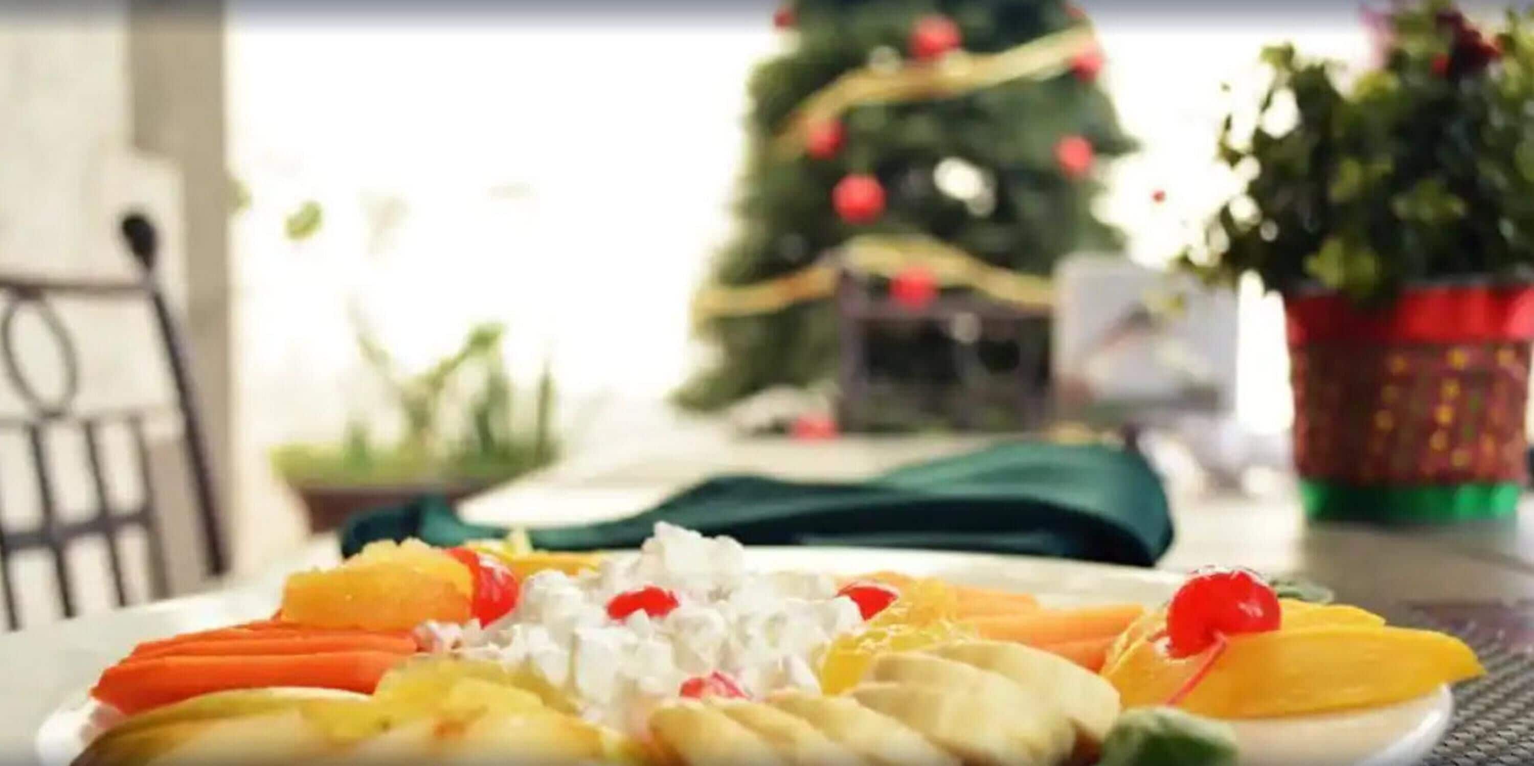 Una mesa de comedor con una bandeja de frutas, un árbol de Navidad al fondo y una planta en maceta.