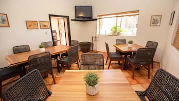 Un comedor con una mesa de madera y sillas de mimbre, un televisor en un estante y cuadros enmarcados en las paredes.
