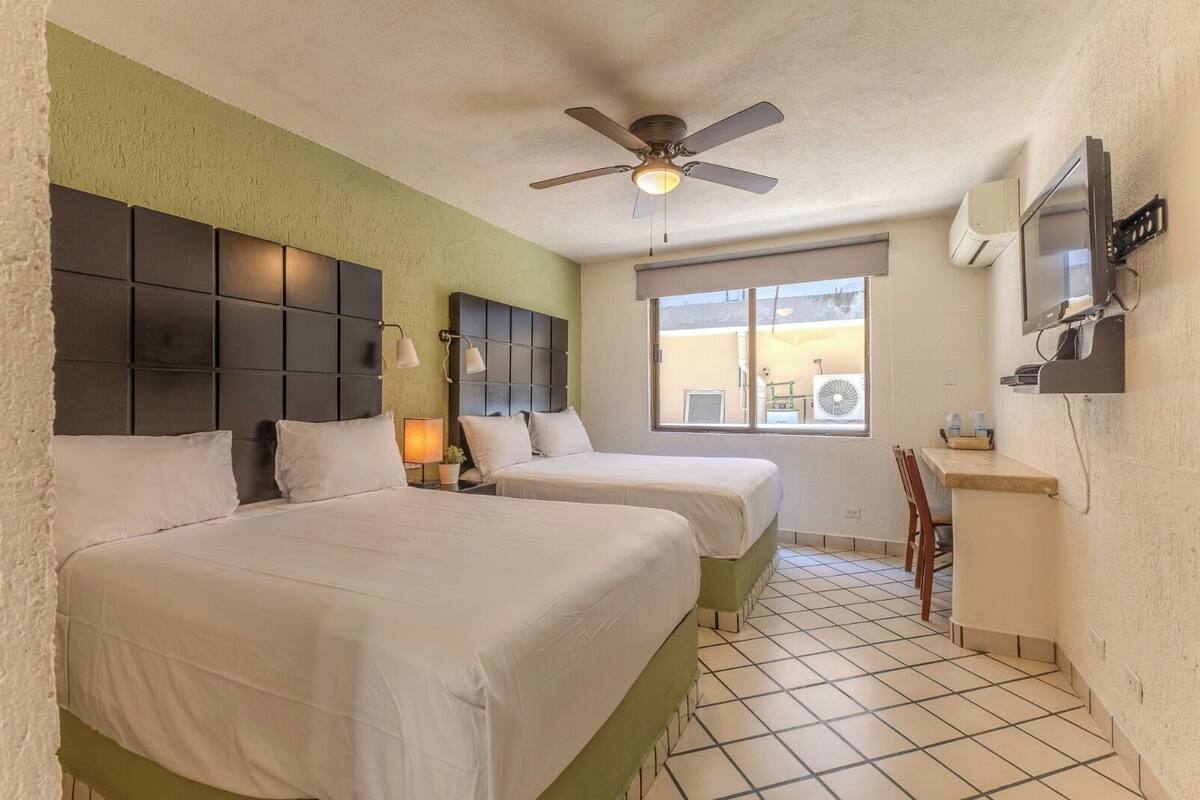 A hotel room with two beds, a ceiling fan, a window with a view, and a TV mounted on the wall.