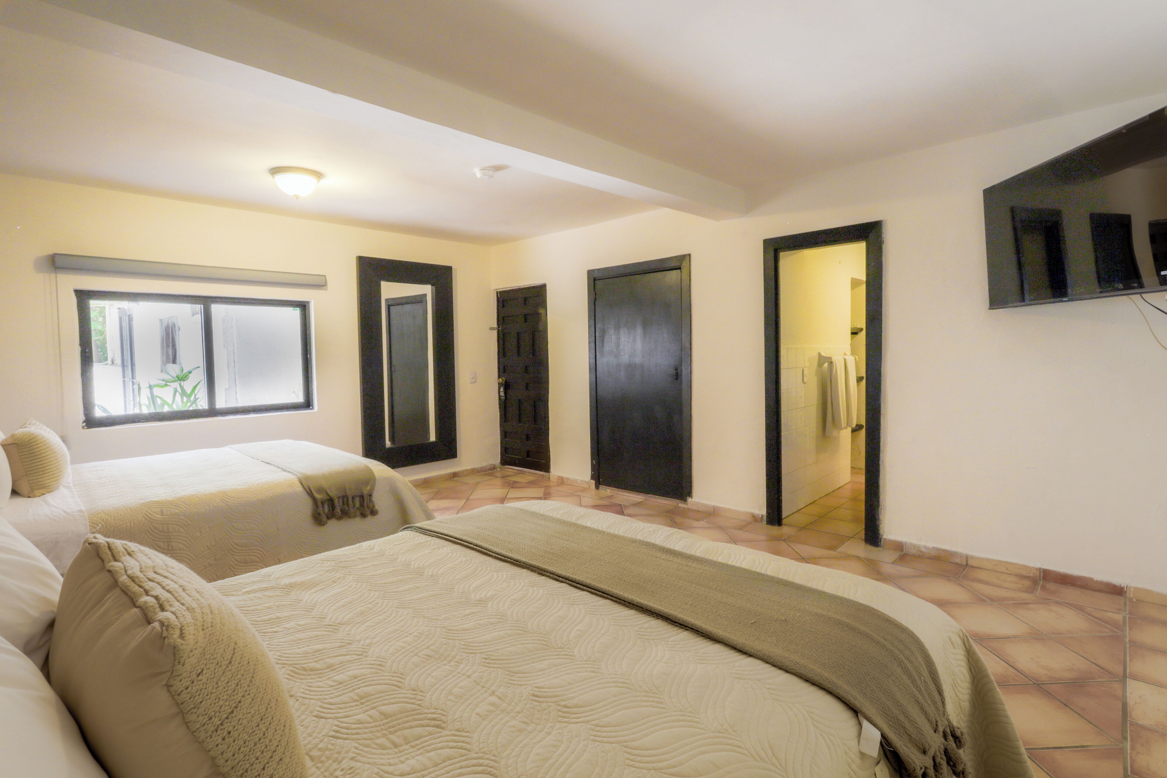 Ein Hotelzimmer mit zwei Betten, einem großen Fenster und einem wandmontierten Flachbildfernseher.