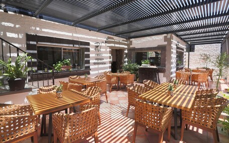 An outdoor patio with wooden tables and wicker chairs, a covered area with a metal roof, and potted plants.
