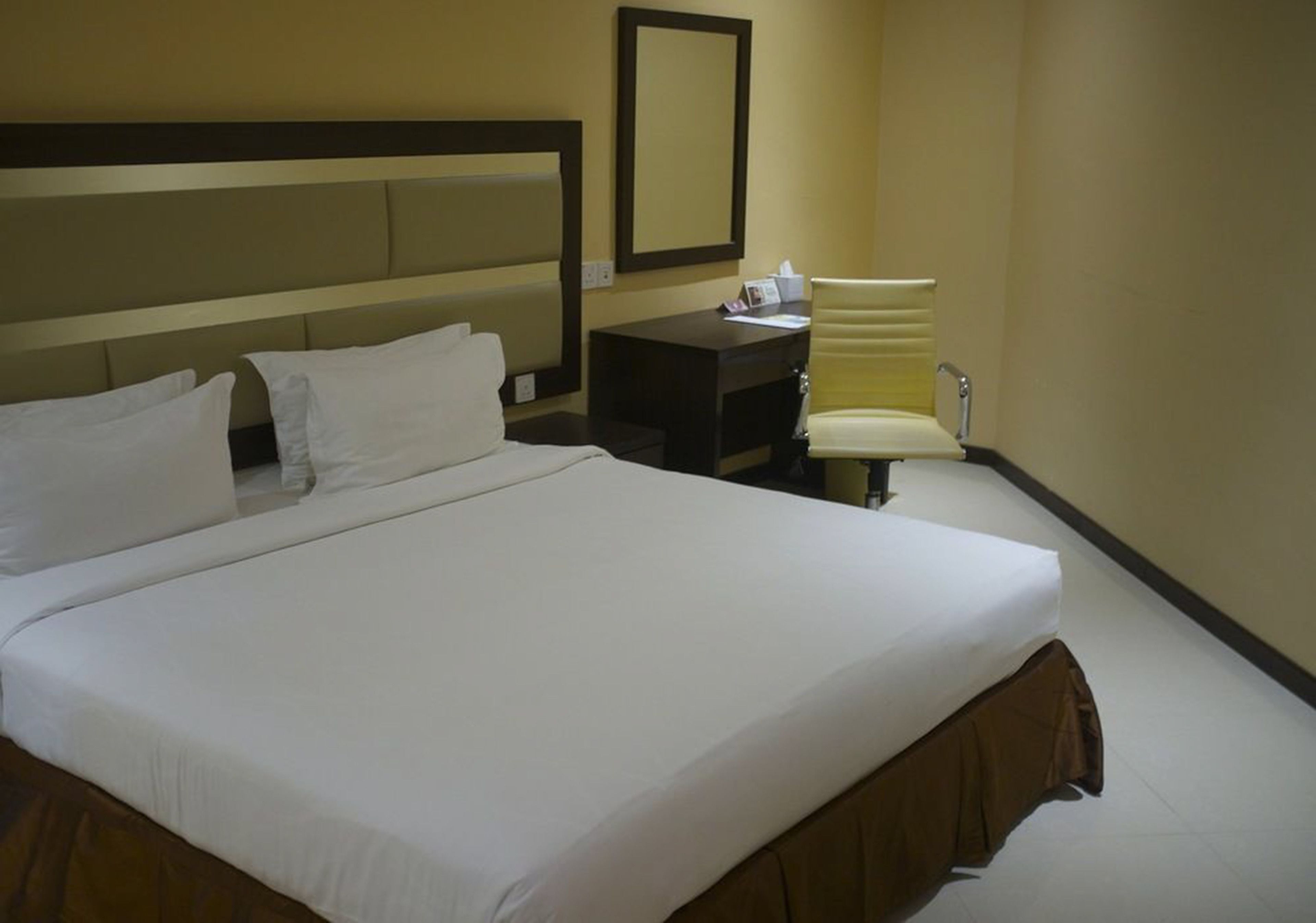 A hotel room with a large bed, a desk, a chair, and a mirror.