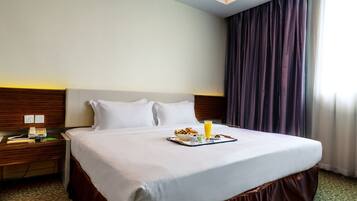 A hotel room with a neatly made bed, a bedside table with a phone and a lamp, and a breakfast tray on the bed.