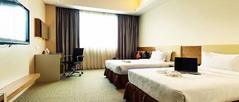 A hotel room with two beds, a desk, a chair, a TV, and a window with curtains.