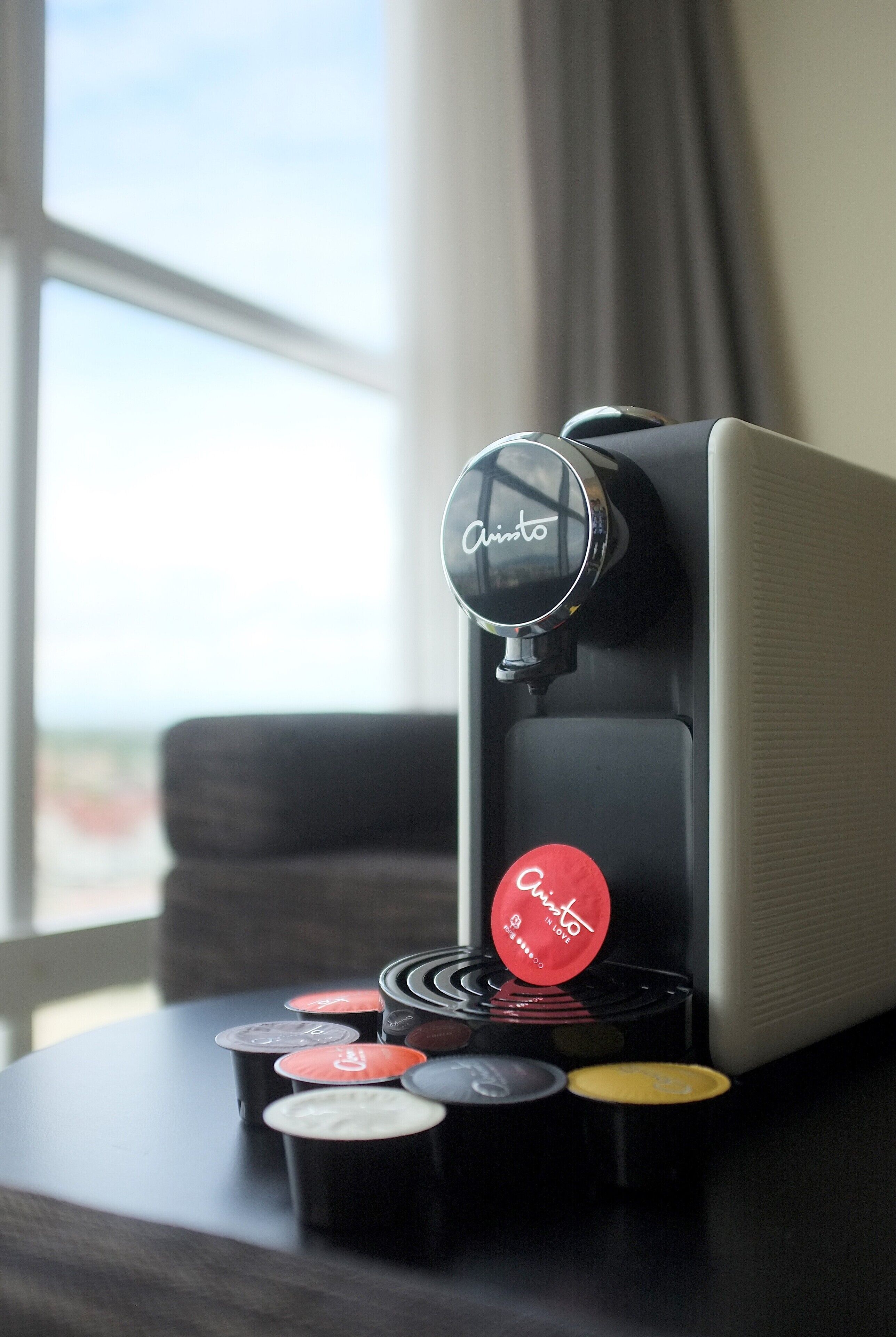 Une machine à café avec plusieurs dosettes de café, posée sur une table près d’une fenêtre.
