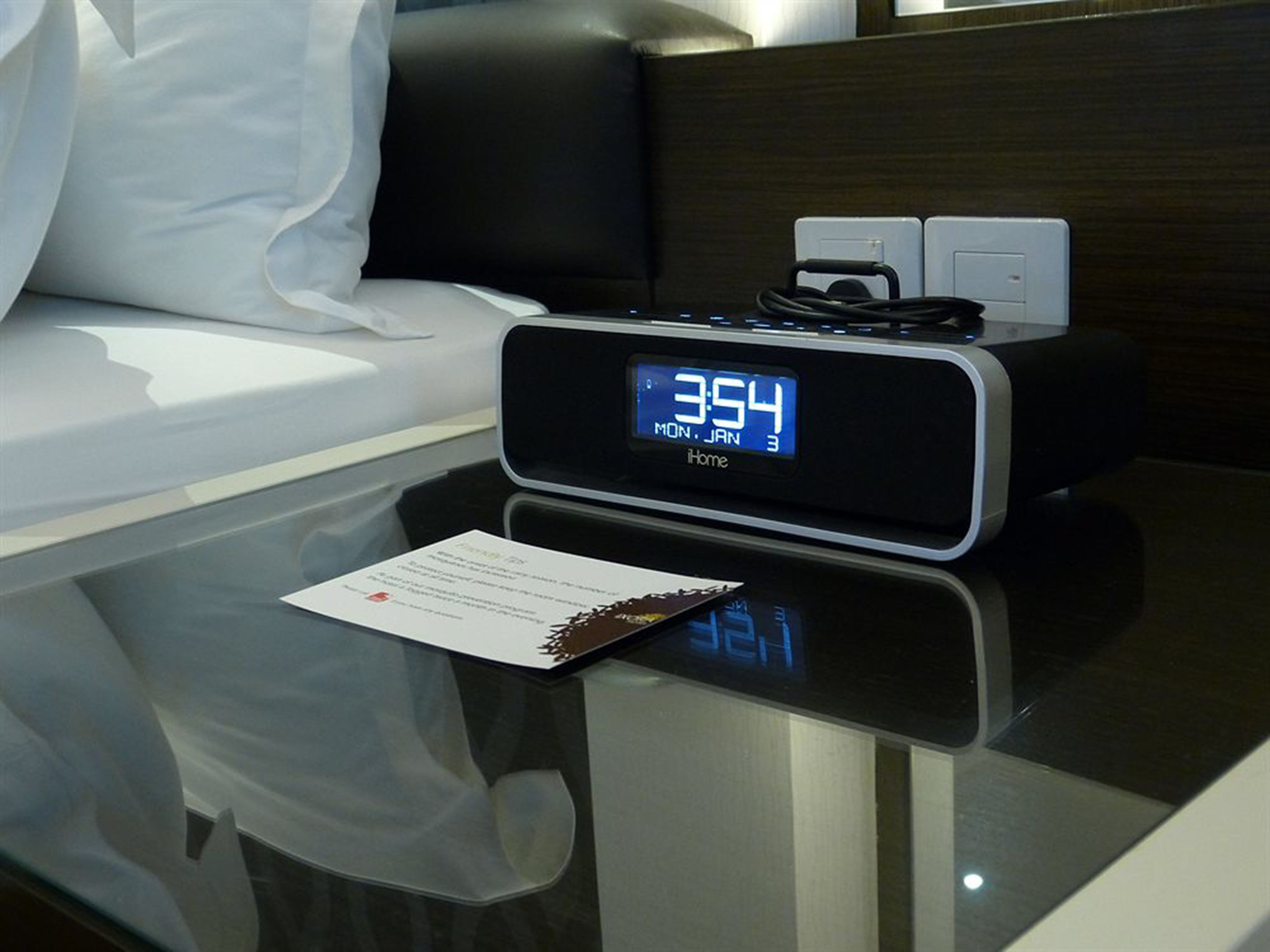 Un reloj digital muestra las 3:54 en una mesita de noche en una habitación de hotel.