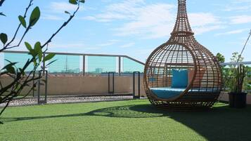 A rooftop terrace with artificial grass, a hanging chair, and a view of the city skyline.