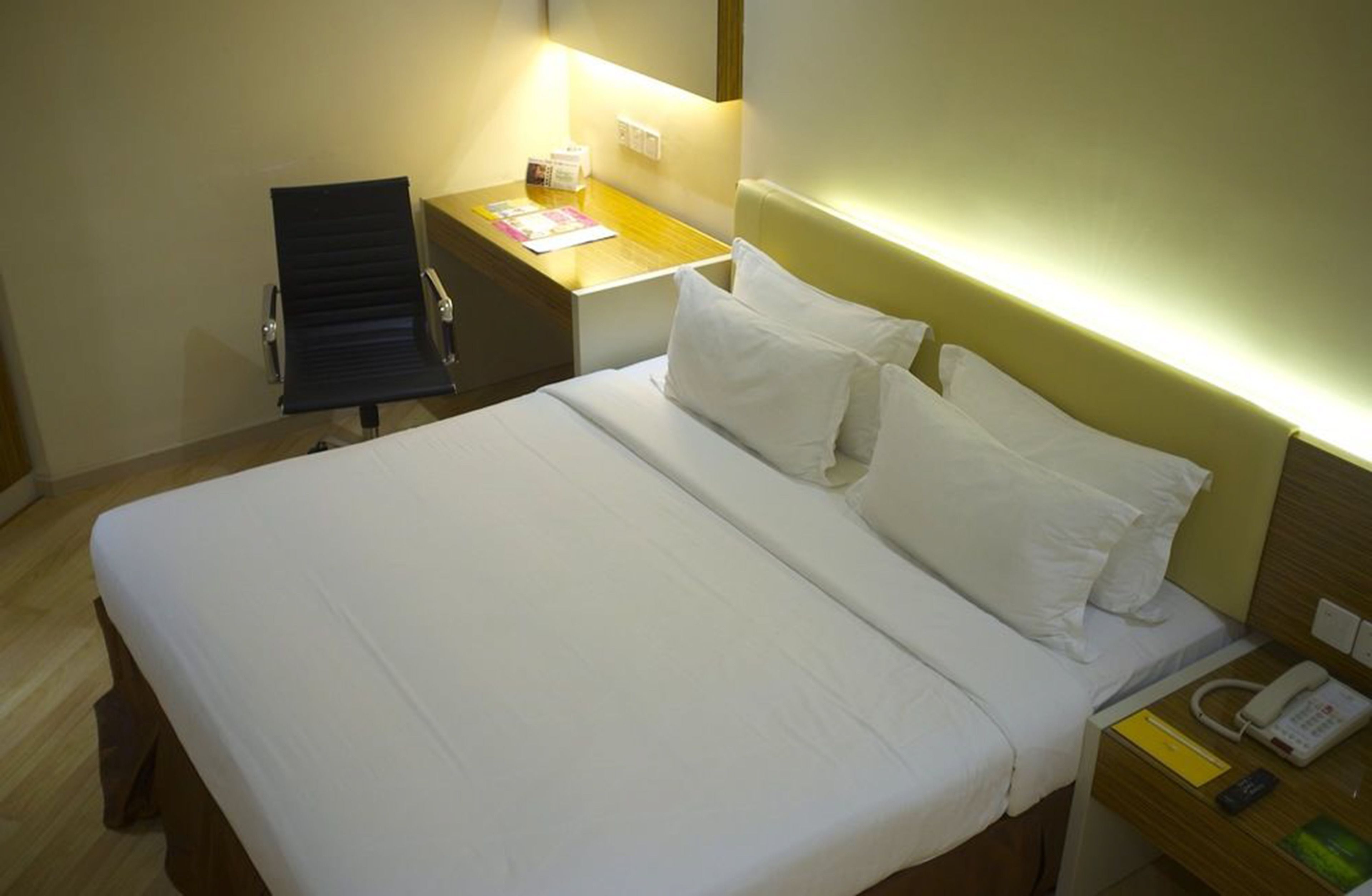 A hotel room with a bed, bedside table, chair, and a desk with a lamp.