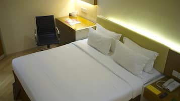 A hotel room with a bed, bedside table, chair, and a desk with a lamp.