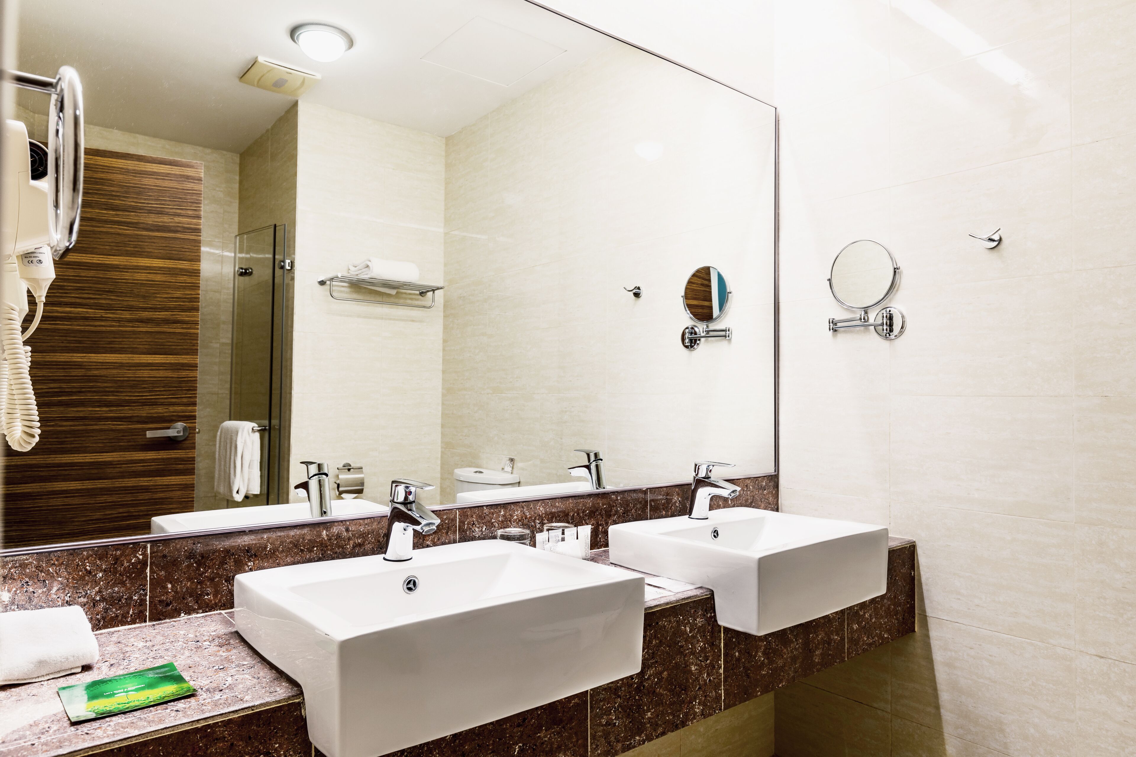 Un baño moderno con dos lavamanos, un espejo grande y un secador de pelo.