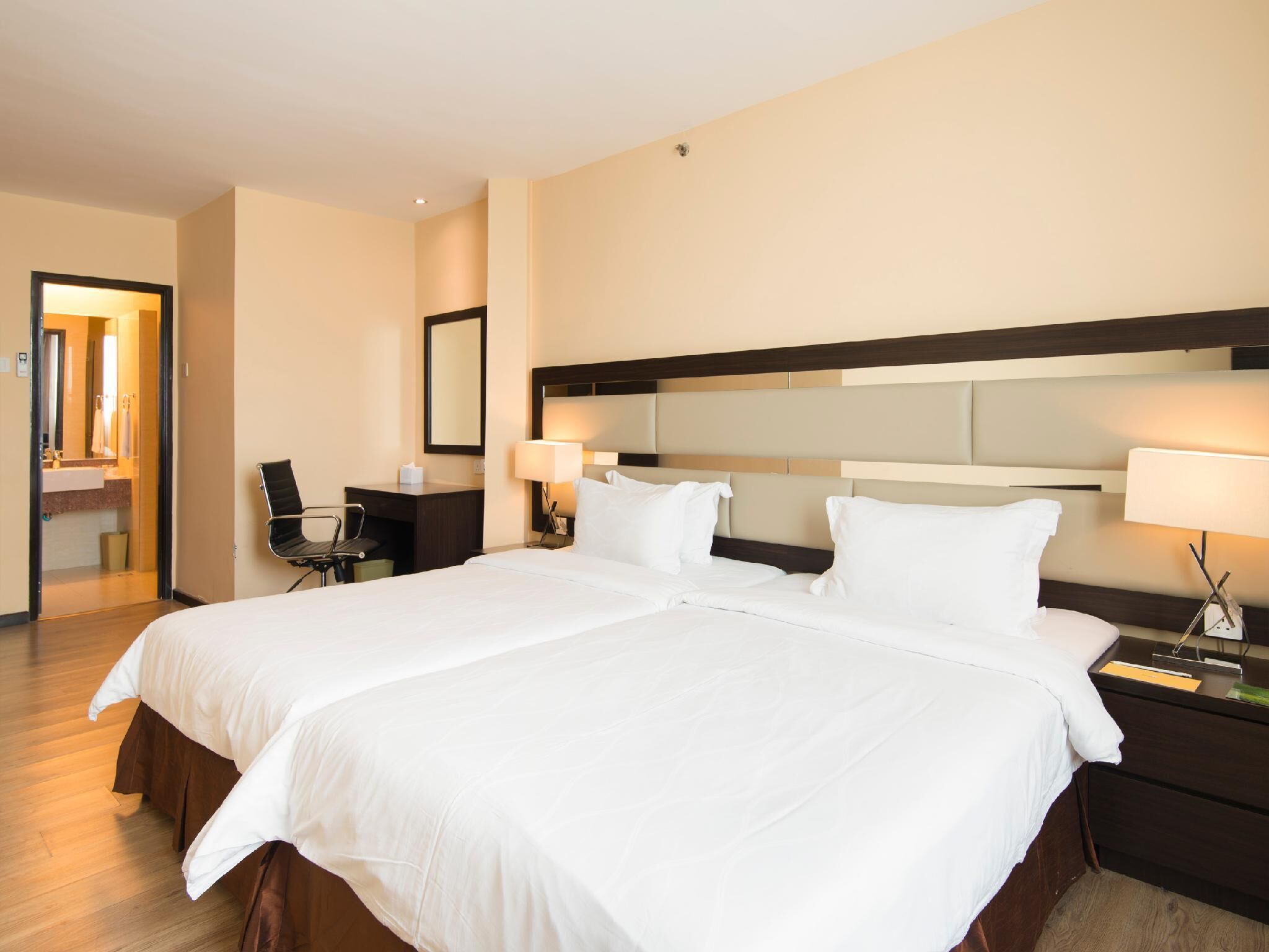 A hotel room with a large bed, two bedside tables with lamps, a desk with a chair, and a mirror on the wall.