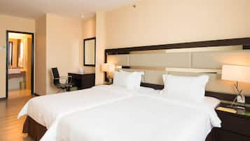 A hotel room with a large bed, two bedside tables with lamps, a desk with a chair, and a mirror on the wall.